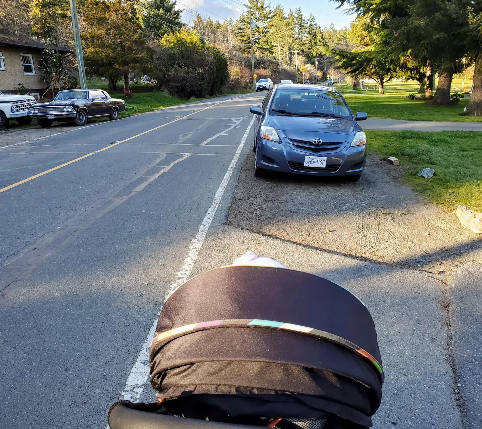 Perspective from a stroller showing a car parked on the unpaved shoulder of Atkins Road, obstructing pedestrian passage