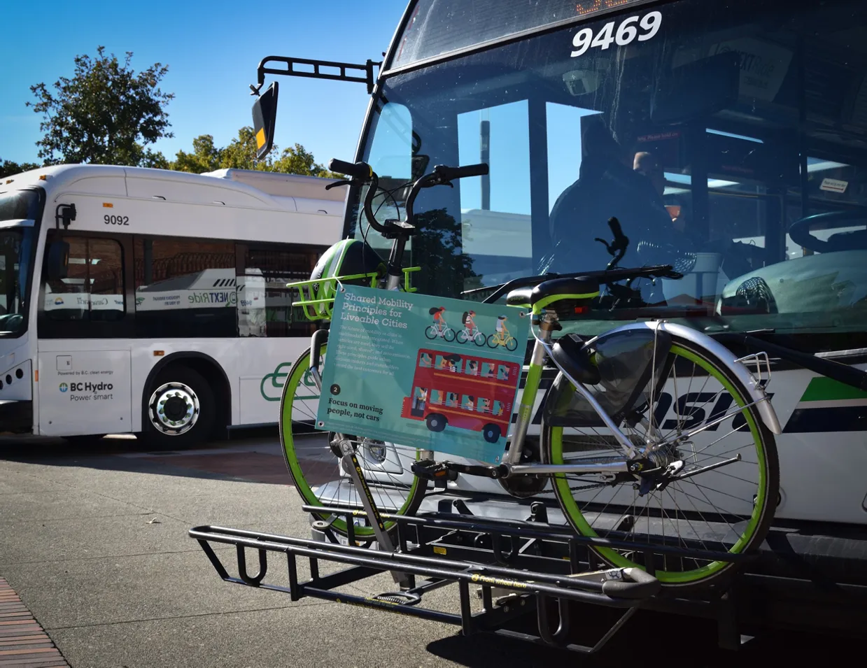 A bicycle mounted on the front rack of a BC Transit bus with a "Shared Mobility Principles" sign