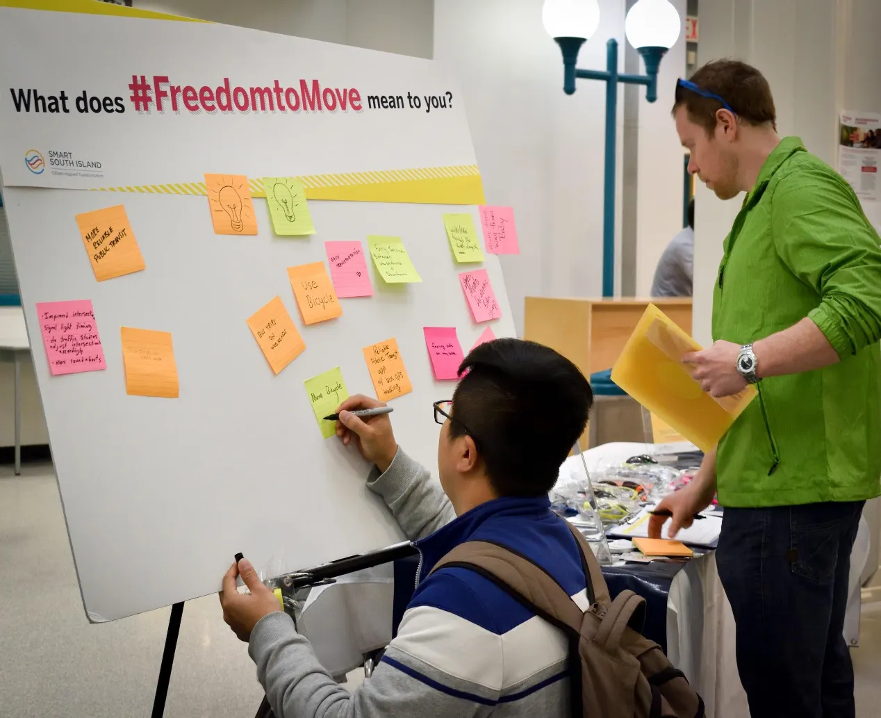 People at a workshop with a whiteboard asking "What does #FreedomtoMove mean to you?" and sticky notes