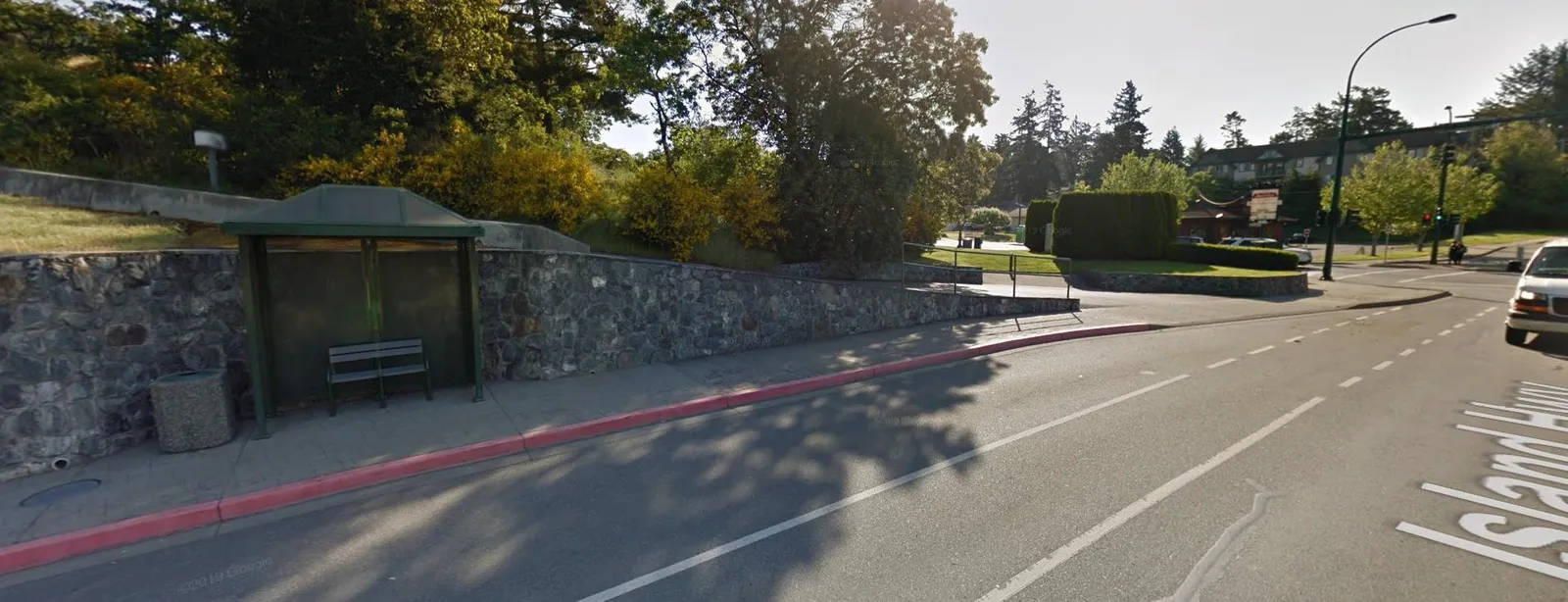 Street view photograph of Island Highway showing a bus shelter, stone wall, and sidewalk