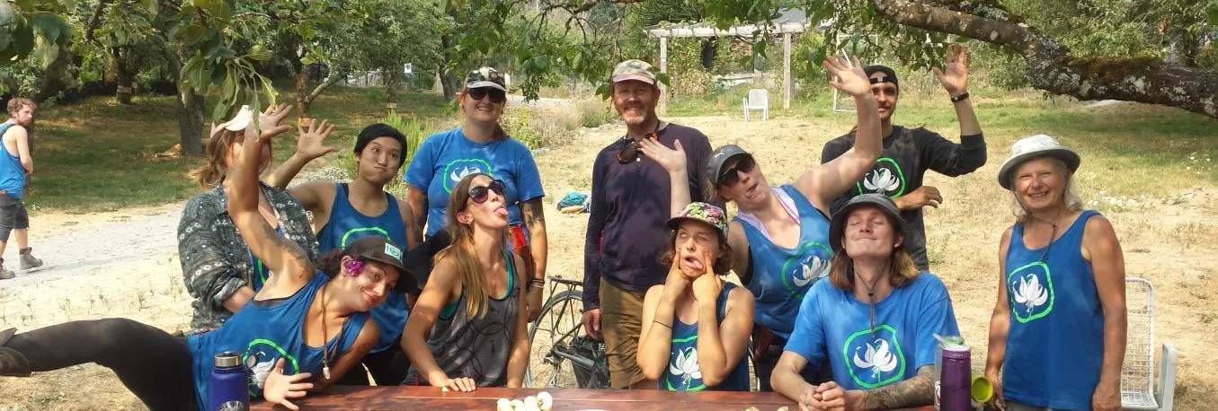 A group of volunteers in matching blue tank tops posing together at a table in the orchard