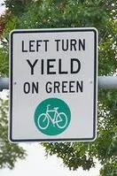 Regulatory sign displaying "LEFT TURN YIELD ON GREEN" with a bicycle symbol