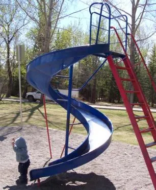 A blue spiral slide on a playground with a child standing nearby