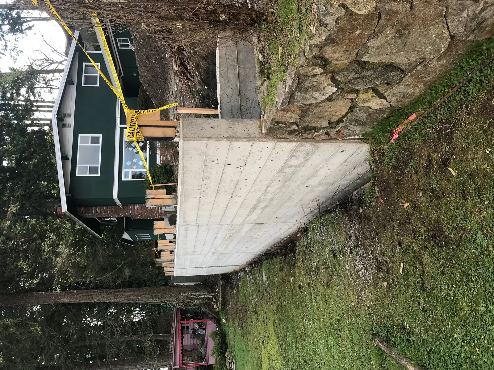 Newly constructed concrete retaining wall in front of a green two-story house with a brick chimney.