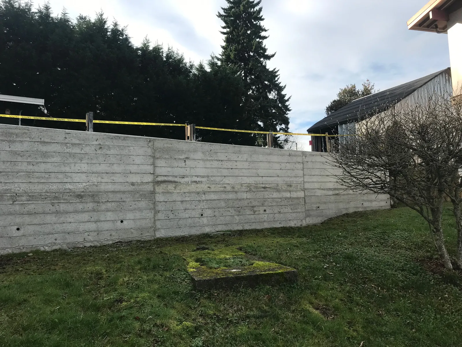 Side profile of the long concrete retaining wall featuring horizontal form marks and drainage holes.