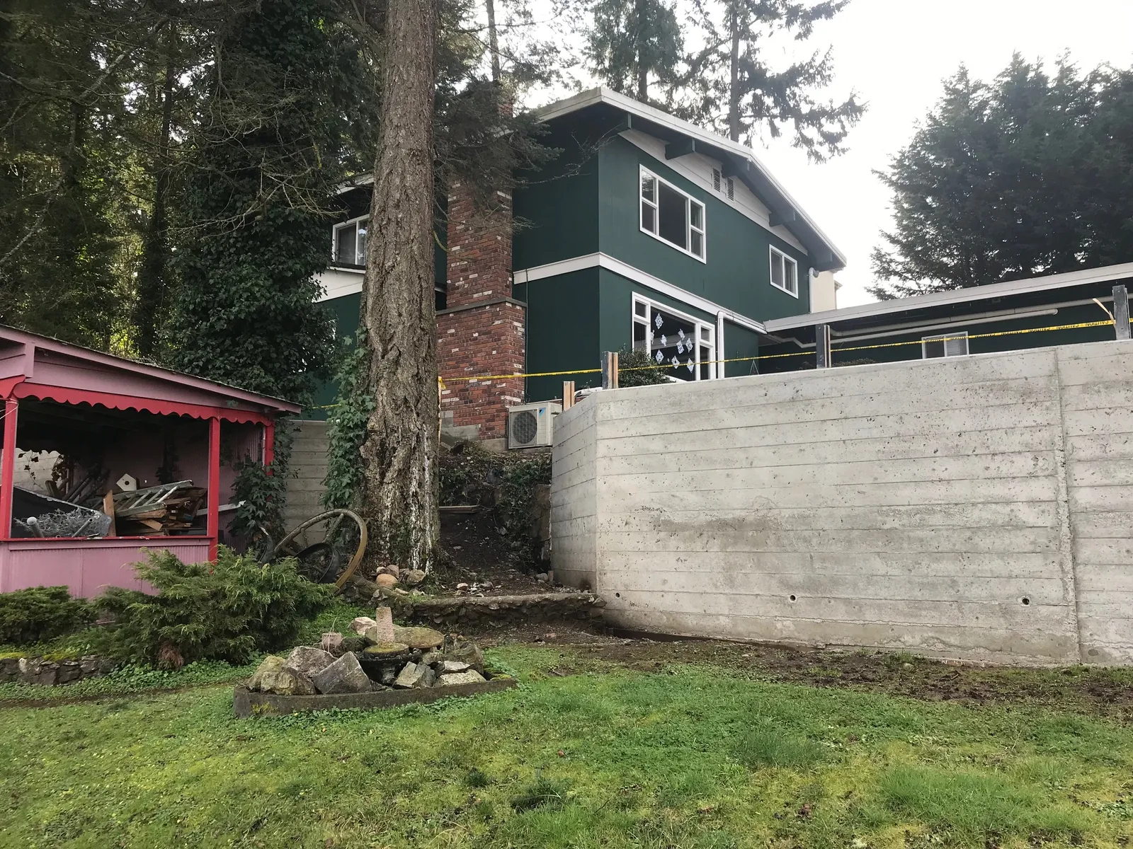 View of the concrete retaining wall with the green house and a pink shed in the background.