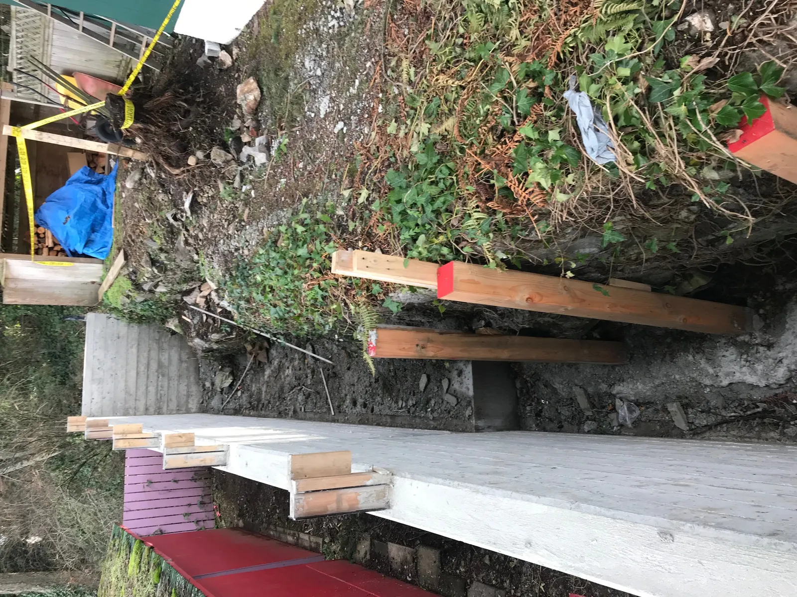 Looking down into the construction trench behind the wall with wooden shoring and a dirt bank.