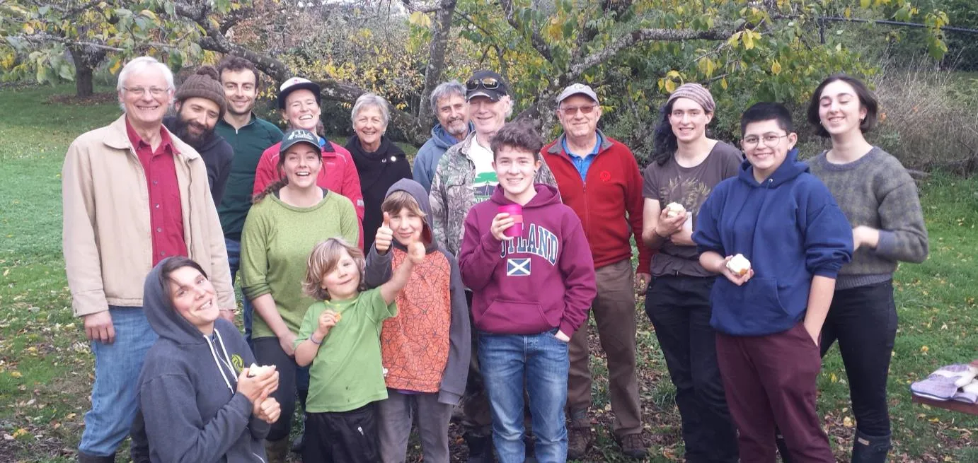 A large group of volunteers of various ages posing for a photo in the orchard