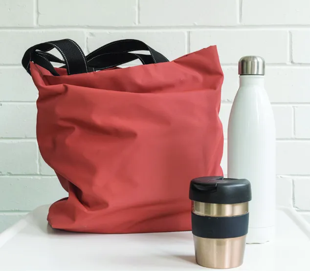 A pink reusable tote bag next to a white water bottle and a reusable coffee cup.