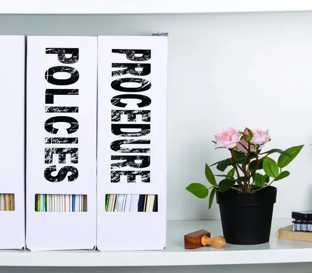 Office binders on a shelf labeled "POLICIES" and "PROCEDURE".