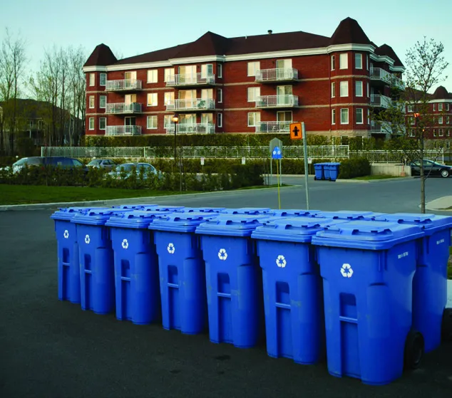 A long row of blue recycling bins outside a large multi-family residential building.