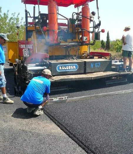 Workers using a paving machine to lay asphalt for a pickleball court surface