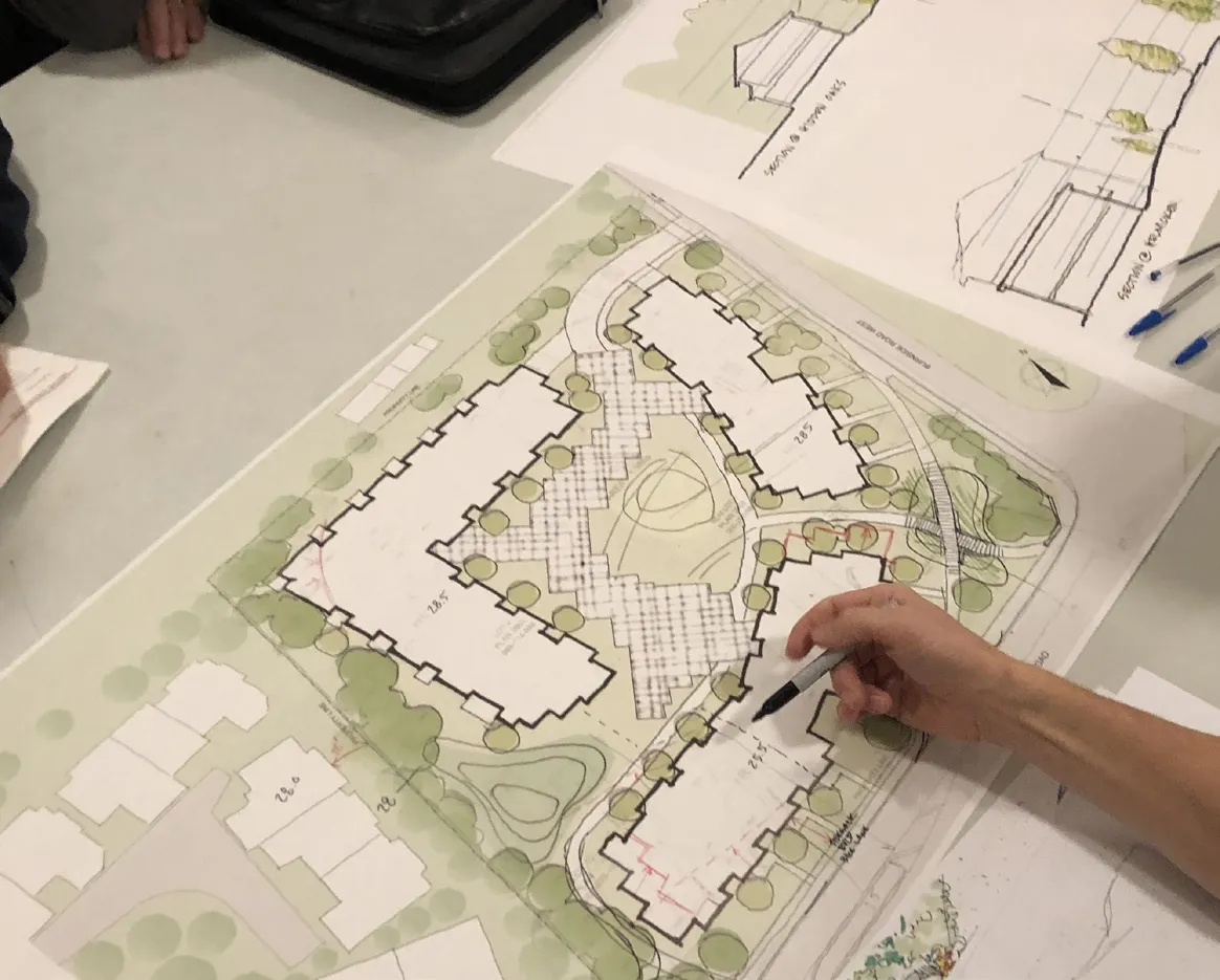 Close-up of workshop attendees' hands pointing to a detailed residential building plan