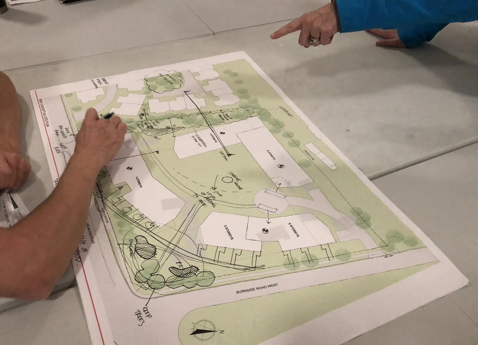 A person pointing at a large conceptual site plan drawing laid out on a table during a planning session.