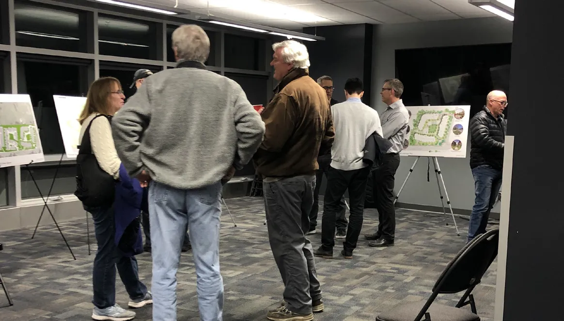 Photo of community members gathered in a meeting room around a table, engaged in a workshop discussion.