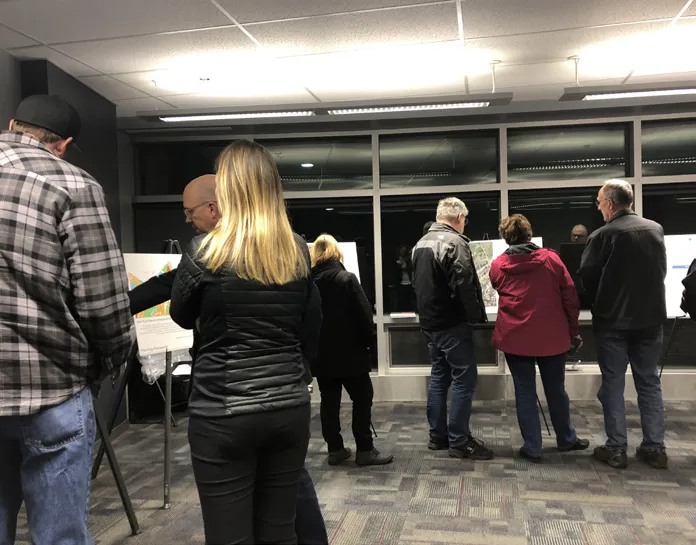 Photo of a group workshop session with participants gathered around tables reviewing large-scale site and landscaping drawings.