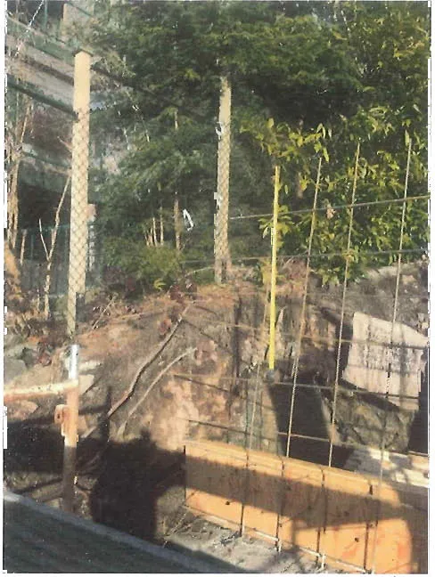 Photo of a concrete footing and rebar in an excavation. Caption: Looking North West at excavated site of proposed Retaining Wall. Concrete footing and exposed rebar shows location of proposed Retaining Wall