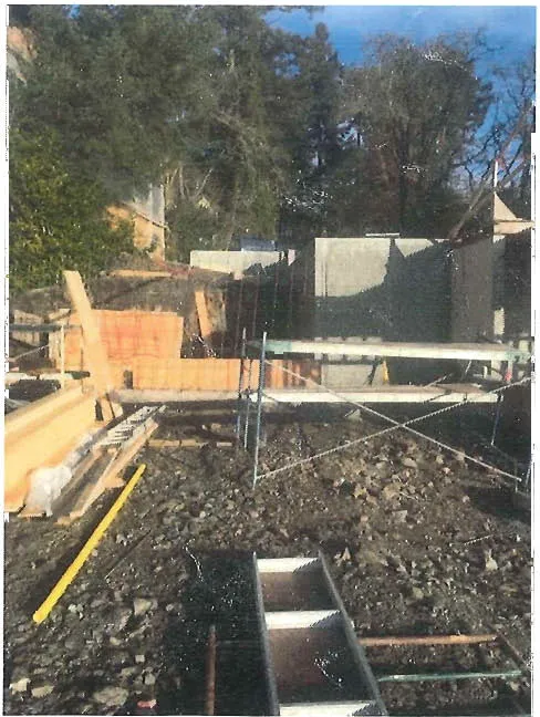 Photo of a construction site with wood forms and a concrete wall. Caption: Looking North at site of proposed flat concrete patio, with proposed Retaining Wall attached to existing residence's new concrete wall behind in the background.