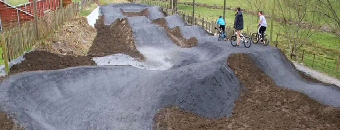 photo of an asphalt pump track with dirt banks and several people with bicycles