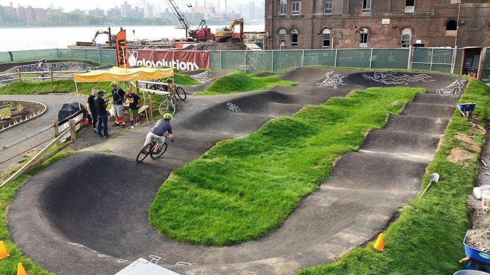 photo of a paved pump track with green grass in the center and a "Velosolutions" banner