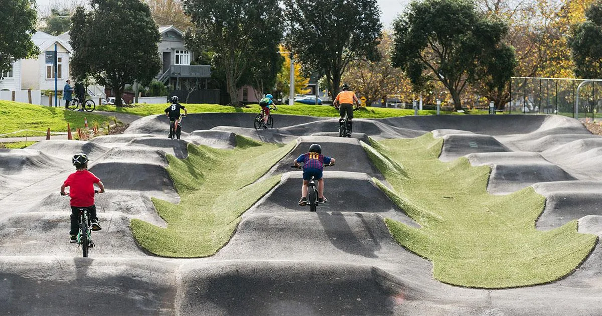 children riding bicycles on a series of asphalt rollers with artificial turf patches