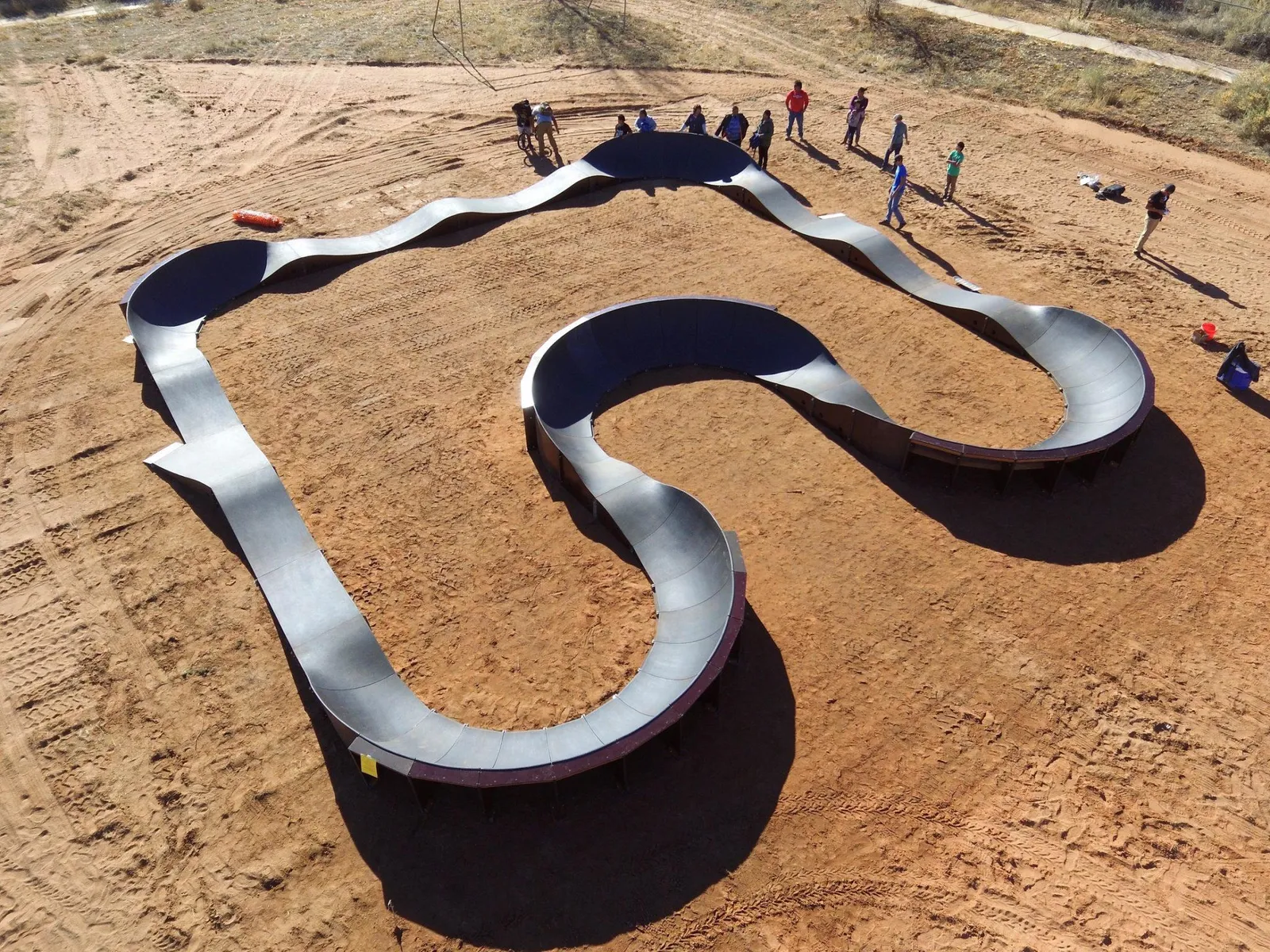 aerial photo of a modular pump track on a dirt surface with people gathered around