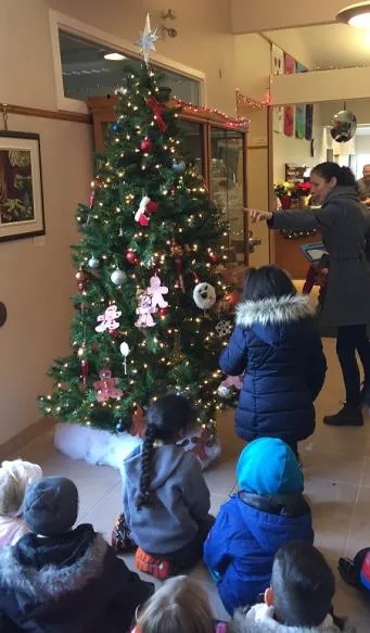 Kindergarten students and a teacher decorating a Christmas tree with homemade ornaments