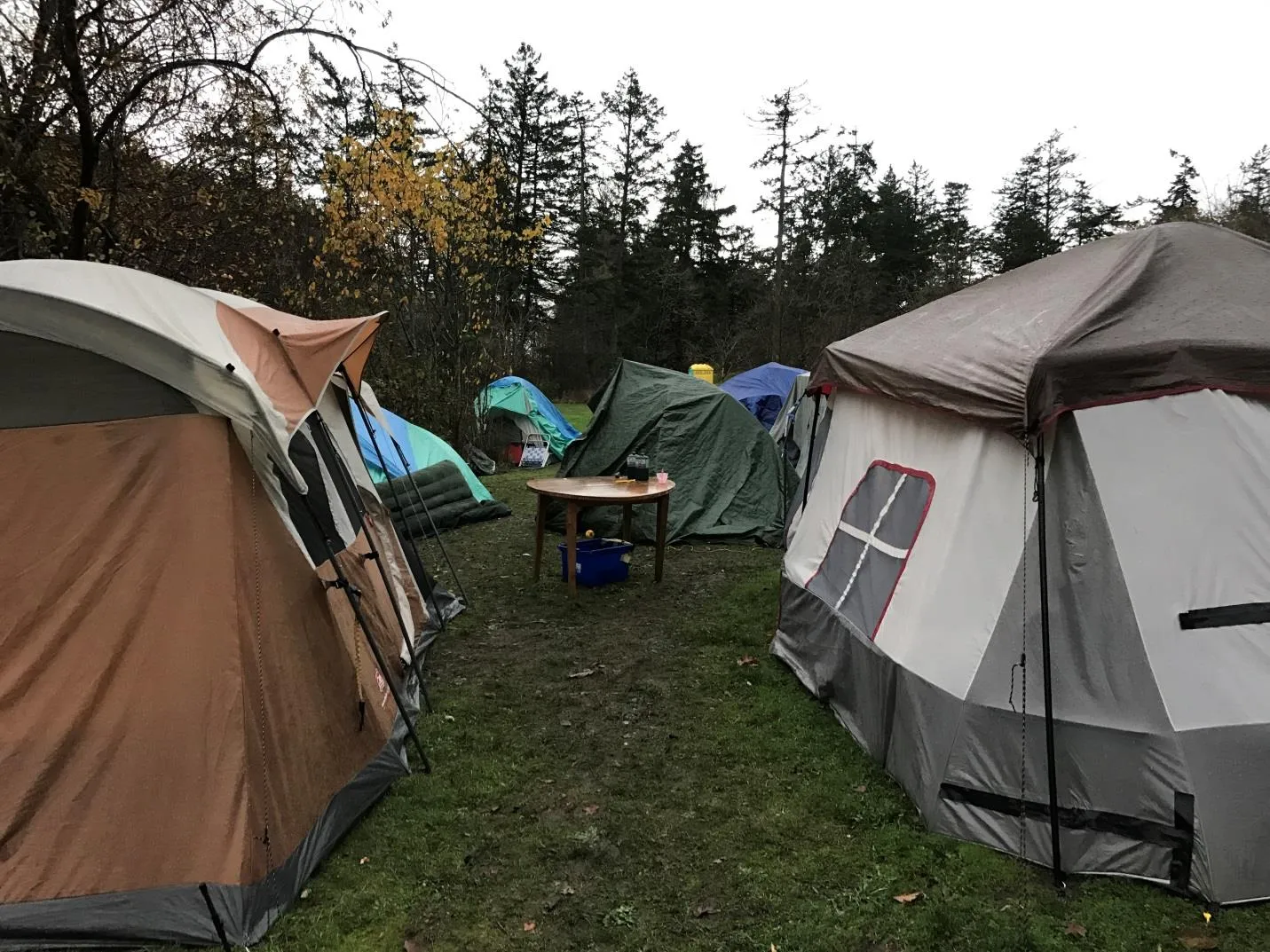 Several large camping tents and a small wooden table at a campsite in Portage Park