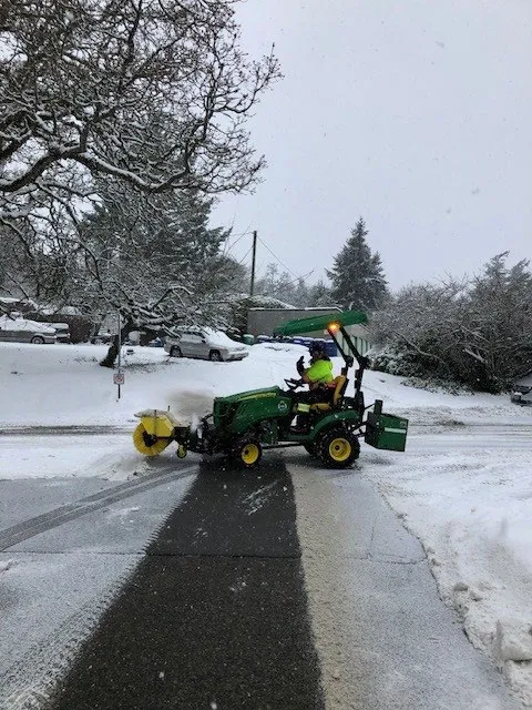 Profile view of Parks Staff operating tractor with sweeper wheel attachment in snow