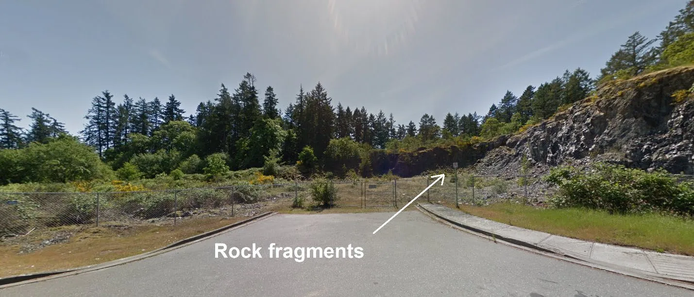 Ground-level photograph of the site entrance indicating the presence of rock fragments and perimeter fencing