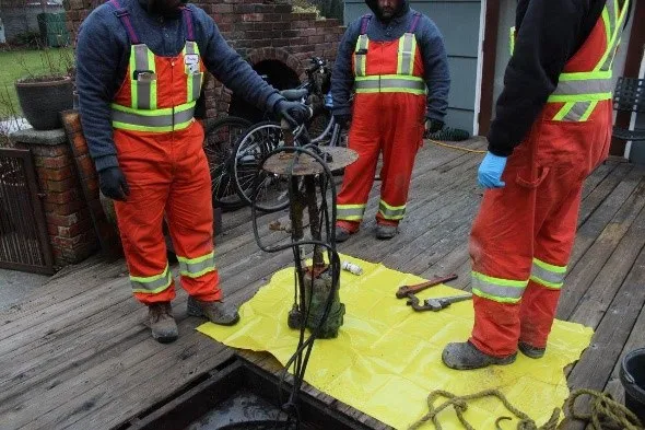 Workers in orange safety gear removing an old grinder pump from an underground access point