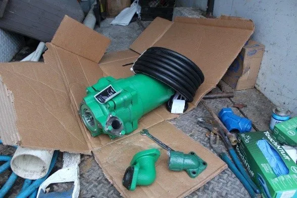 A new green grinder pump and replacement components laid out on cardboard for installation
