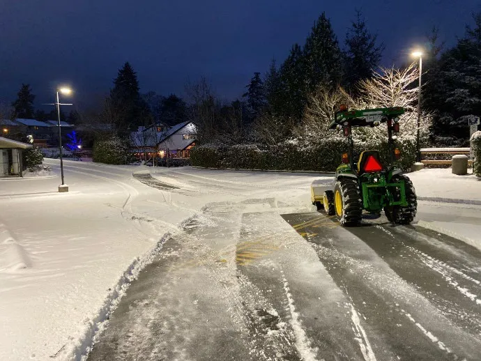 A tractor clearing snow from a parking lot at night under streetlights