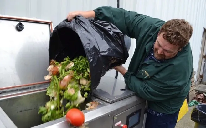 photo of a man emptying a black bag of organic food waste into a composting bin