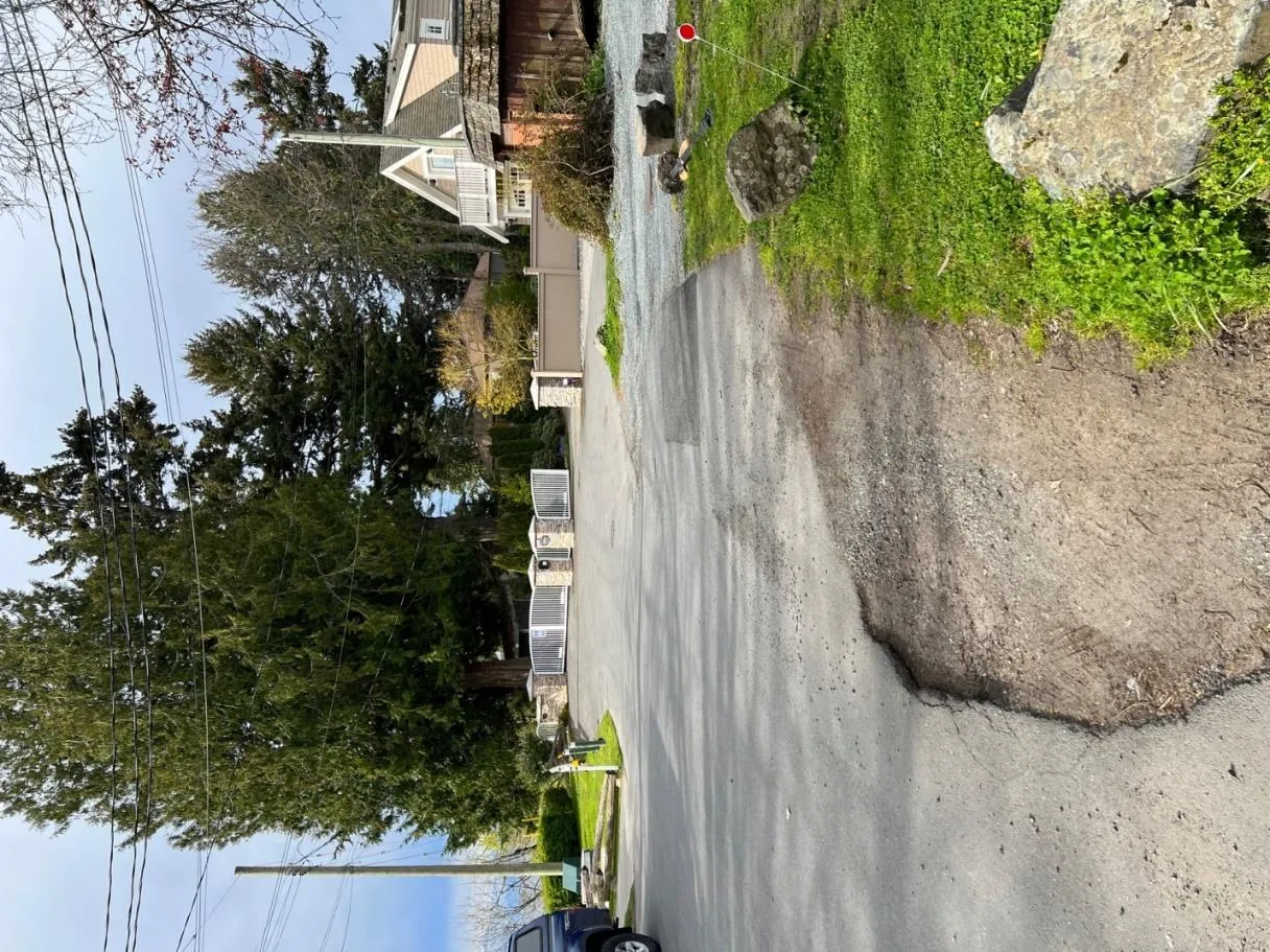 Paved road with a gravel patch on the edge, leading towards a gated residential entrance