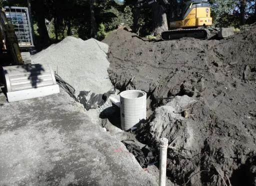 Construction site at the midpoint of the driveway showing a concrete manhole and excavated earth