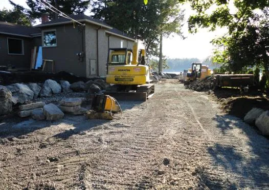 Large excavator on a levelled gravel area near a residential building