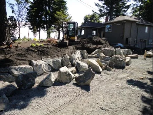 Row of large rocks being placed for a retaining wall with an excavator nearby