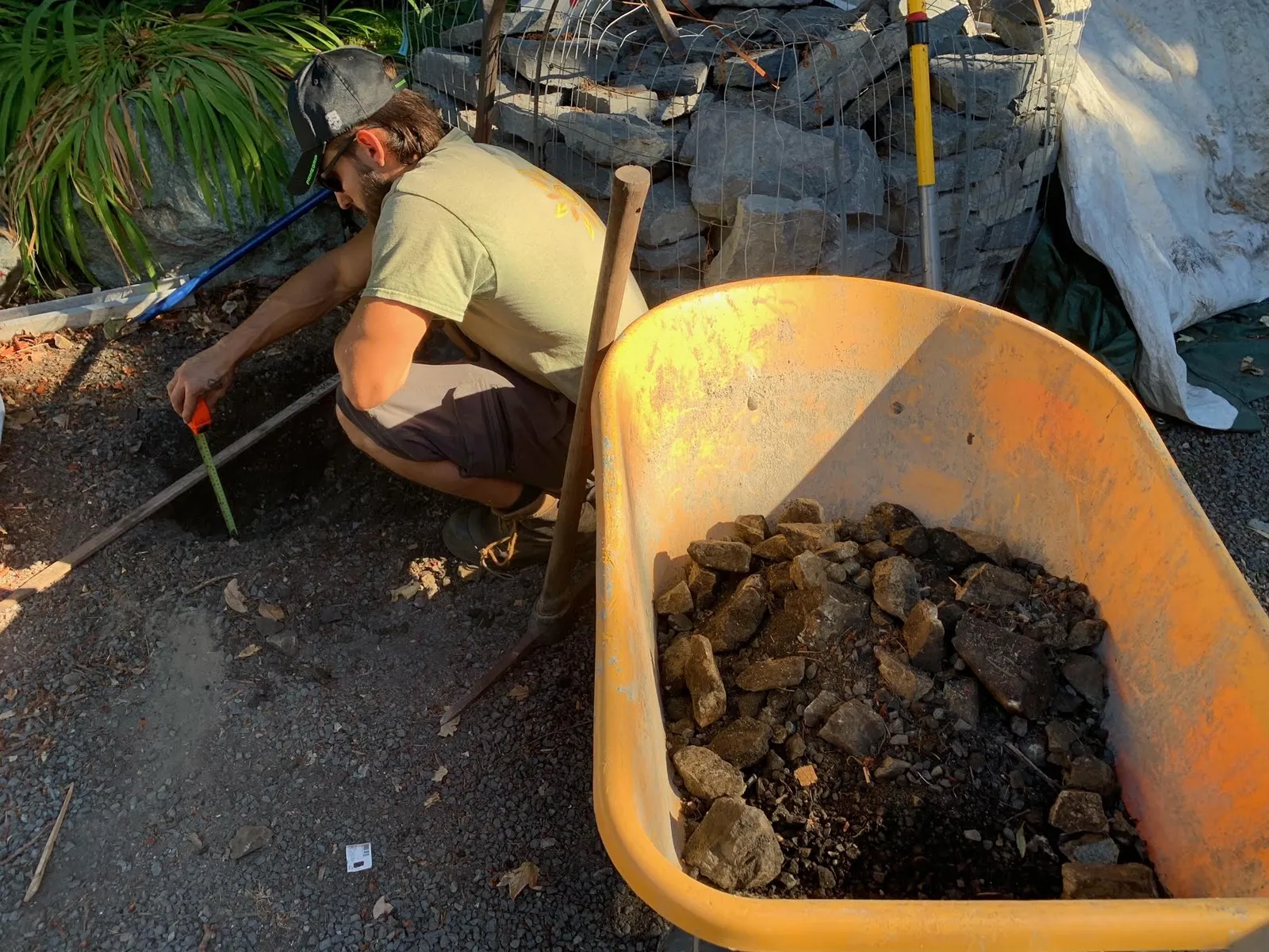 Worker crouched over a hole, measuring depth with a tape measure next to a wooden board