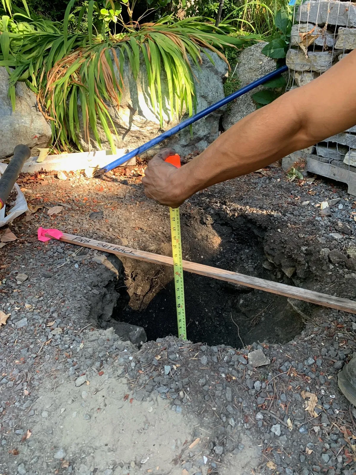 Vertical close-up of a hole in the ground with a tape measure showing depth increments