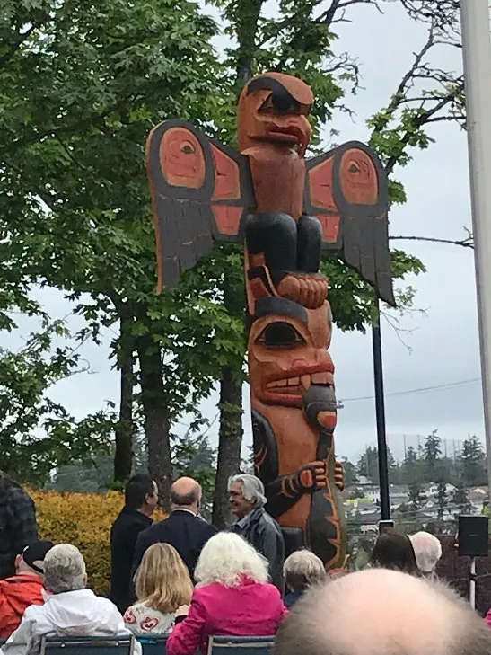 Unveiled totem pole with artist T. LaFortune standing to the right