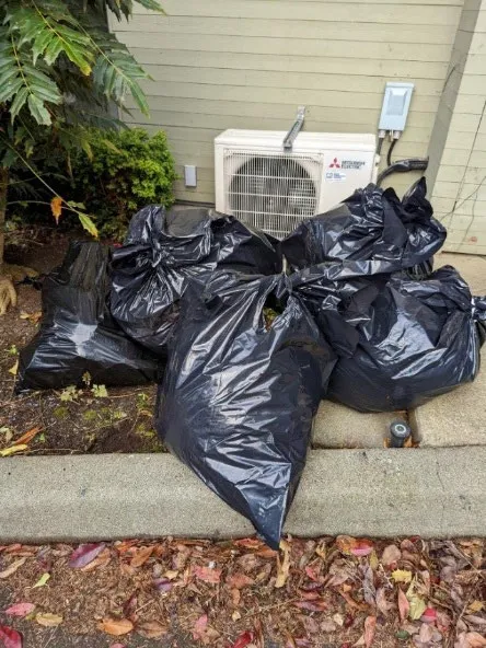 Several black garbage bags of compost material dumped in a parking lot