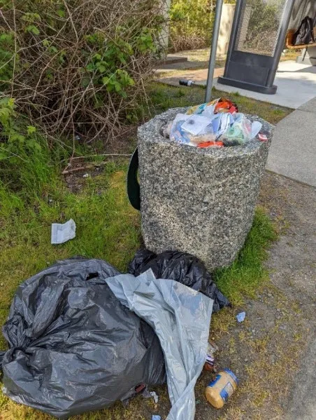 Overfilled stone refuse container with garbage bags on the ground