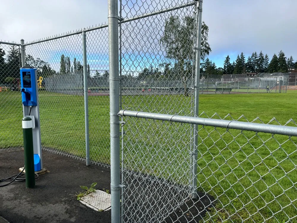 Photo of an electric vehicle charging station in a park setting near a chain-link fence