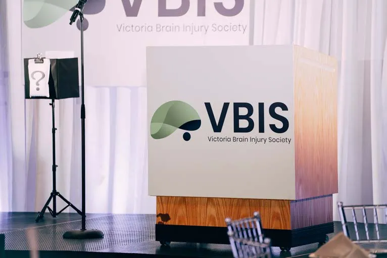 Man with a name tag standing beside a VBIS information banner
