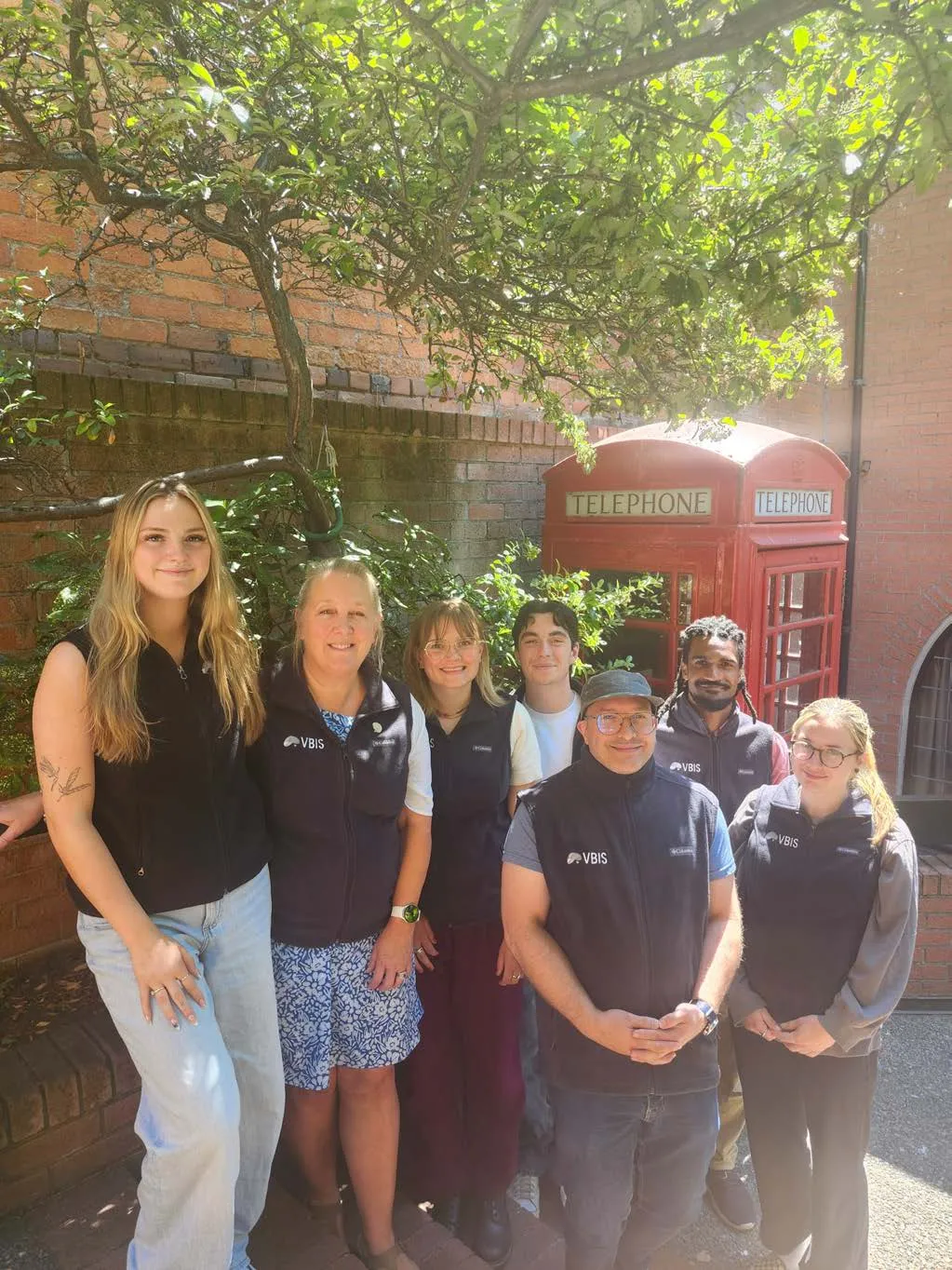A group photo of the VBIS staff standing in front of red telephone booths