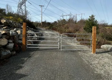 A new metal gate installed across a gravel road access point