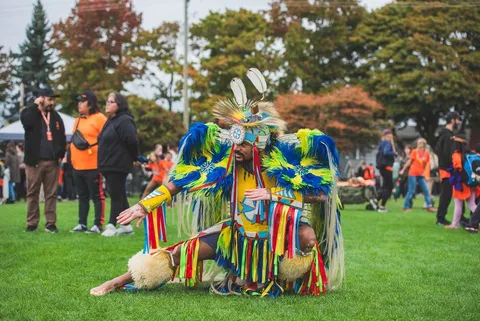 A dancer wearing vibrant blue and yellow regalia performing on grass