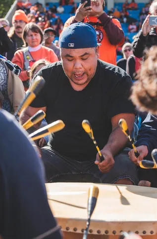 A person wearing a blue baseball cap playing a traditional drum