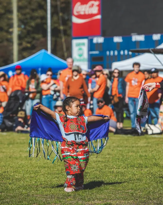 A young child wearing traditional regalia dancing on a field